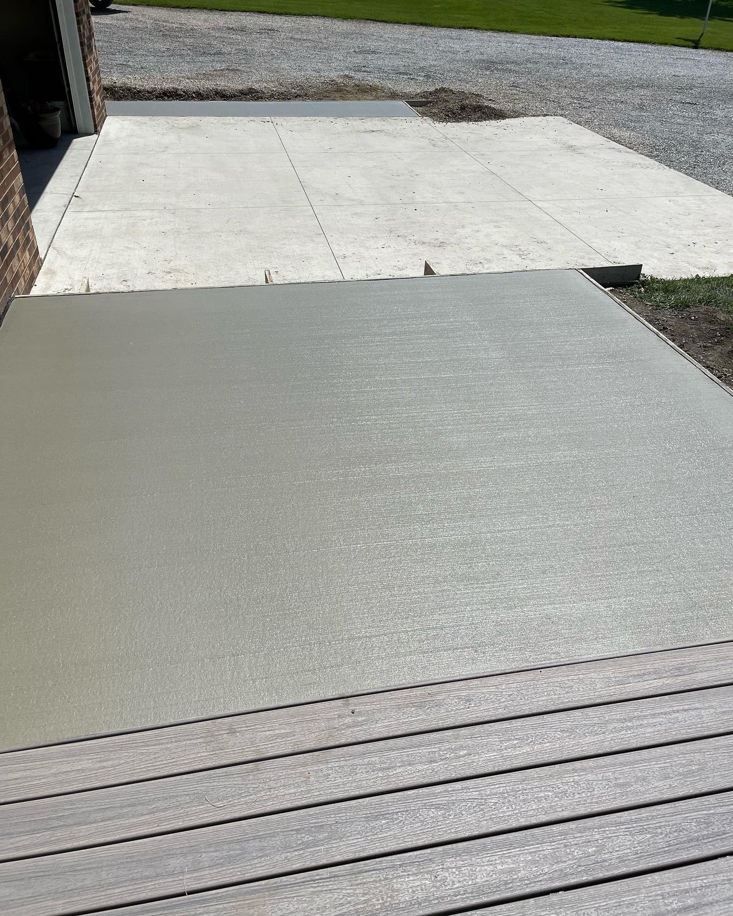 Fresh broom-finished concrete patio next to a wood deck